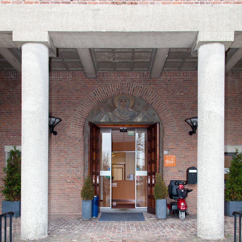 Hoofdingang tussen twee betonnen zuilen onder een boog van baksteen