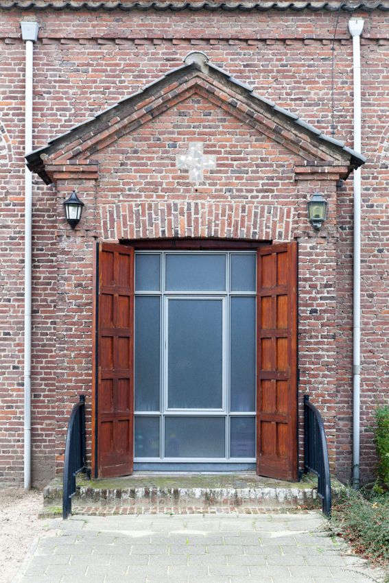 Zijingang met openstaande houten deuren onder een bakstenen fronton